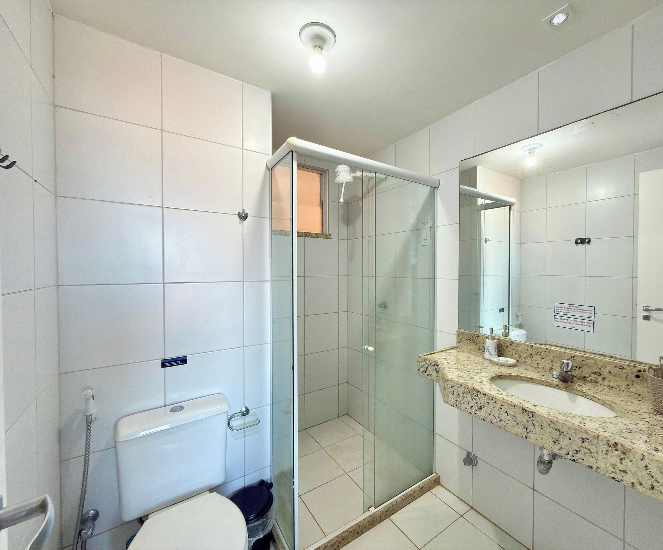 A modern bathroom with a glass shower enclosure, a toilet, and a granite countertop sink.