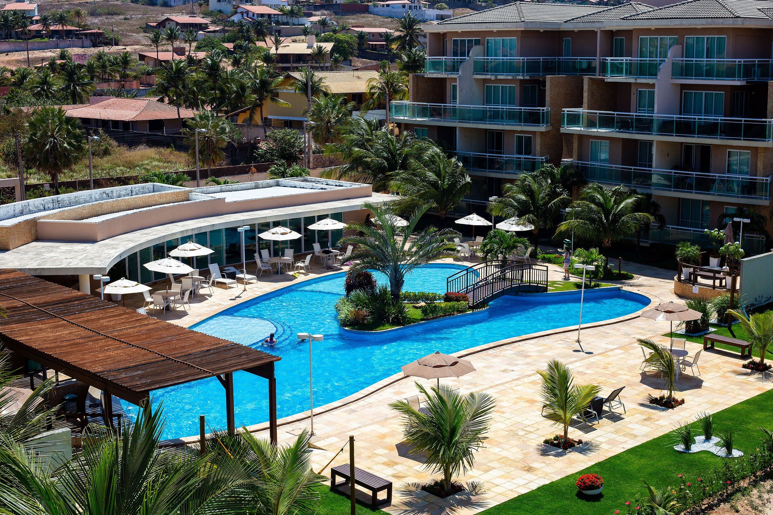 A resort with a swimming pool, lounge chairs, and palm trees.