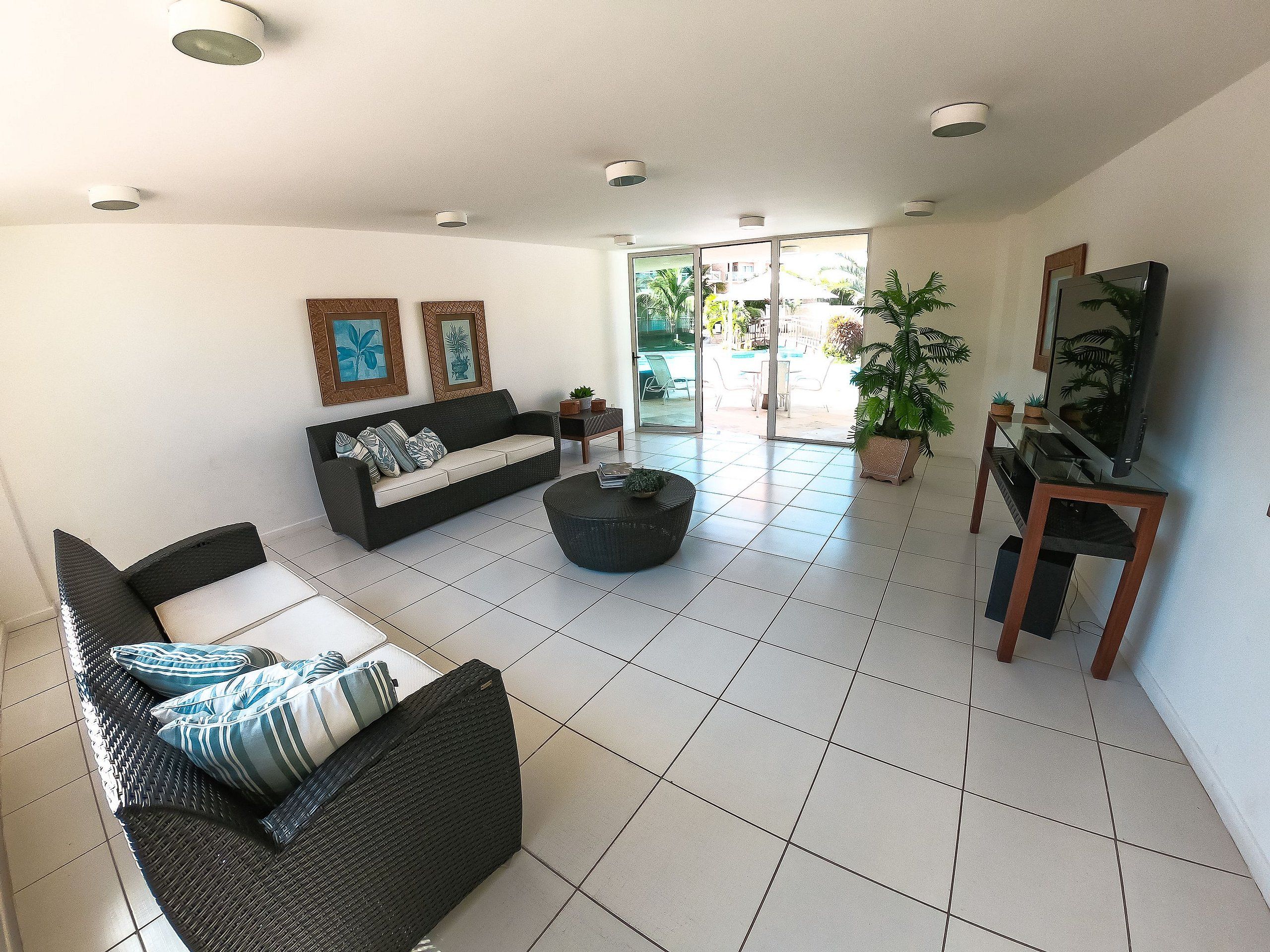 Un salon comprenant un canapé, une table basse, un téléviseur posé sur un meuble et une porte donnant sur un balcon.