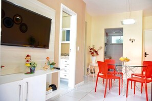 A modern kitchen with white cabinets, a dining area with red chairs, and a small table with a vase of flowers. - Palm Beach Porto das Dunas - CE (Aquiraz)