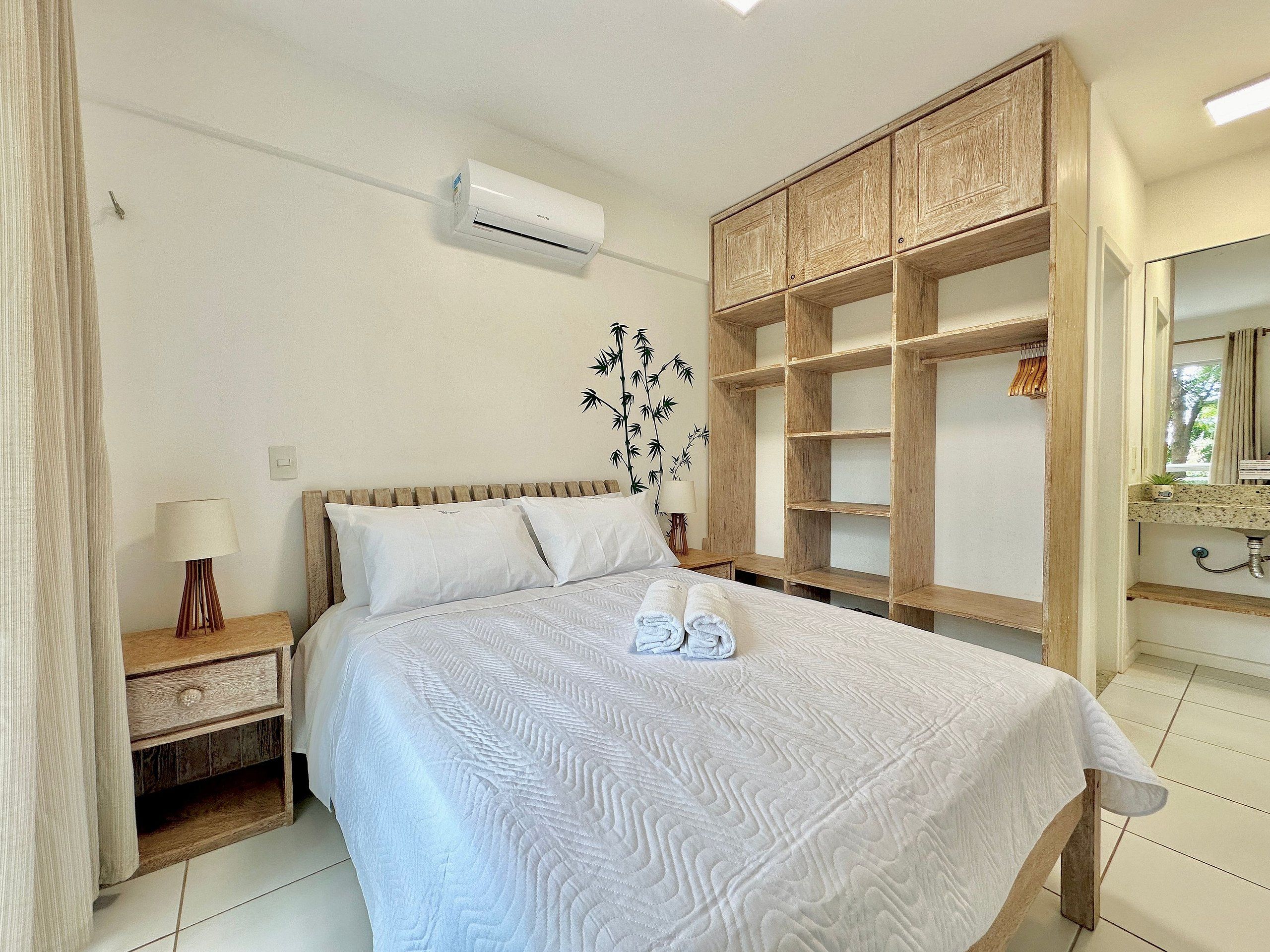 Un dormitorio ordenado con cama, mesita de noche, espejo y armario de madera.