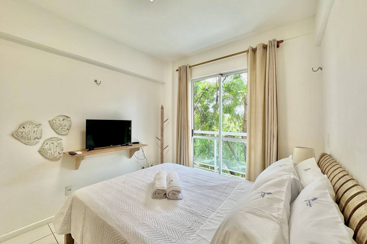A bedroom with a bed, a TV on a shelf, a window with curtains, and wall art.