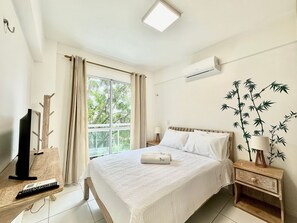 Een slaapkamer met een bed, nachtkastje, lamp en een televisie op een houten standaard.