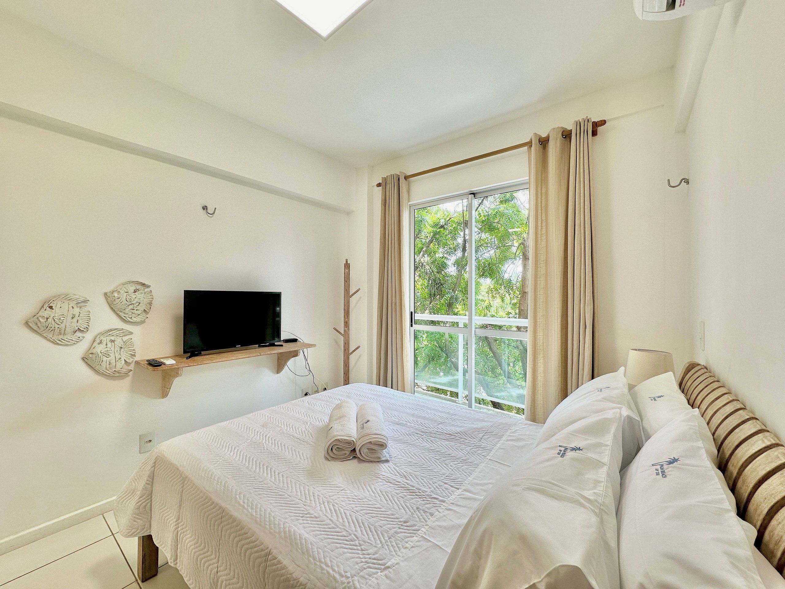 Quarto com cama, TV em uma prateleira, janela com cortinas e obras de arte nas paredes.