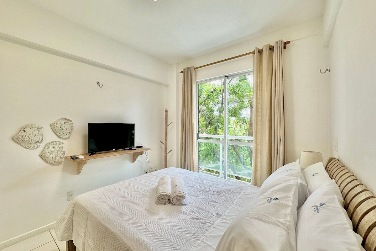 A bedroom with a bed, a TV on a shelf, a window with curtains, and wall art.
