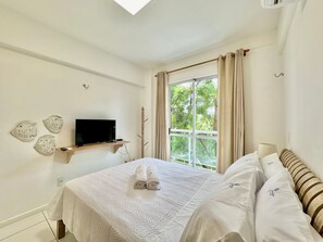 A bedroom with a bed, a TV on a shelf, a window with curtains, and wall art.