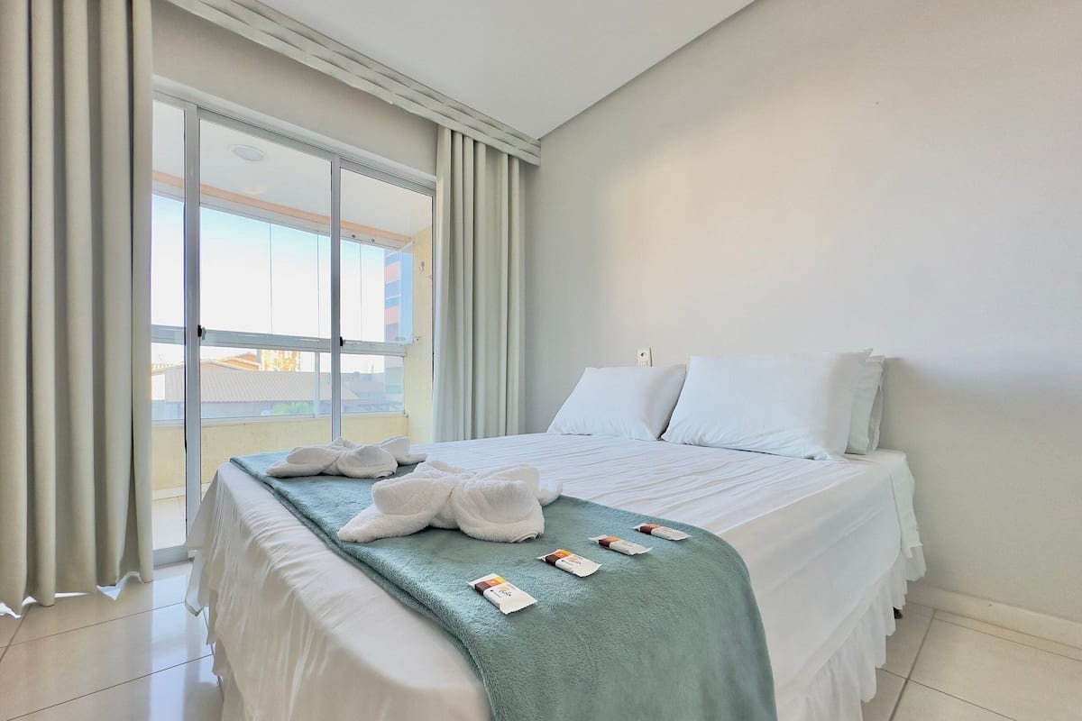A hotel room with a bed, a green blanket, white pillows, and a window with curtains.