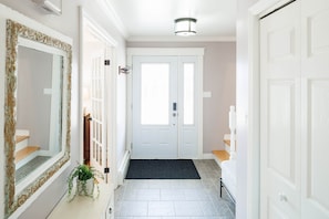 A hallway with a double door, a doormat, a potted plant, and a mirror. - Lewis Point Charlottetown Retreat (Charlottetown)