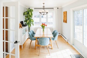 A dining area with a wooden table, blue chairs, a potted plant, and a vase with flowers. - Lewis Point Charlottetown Retreat (Charlottetown)