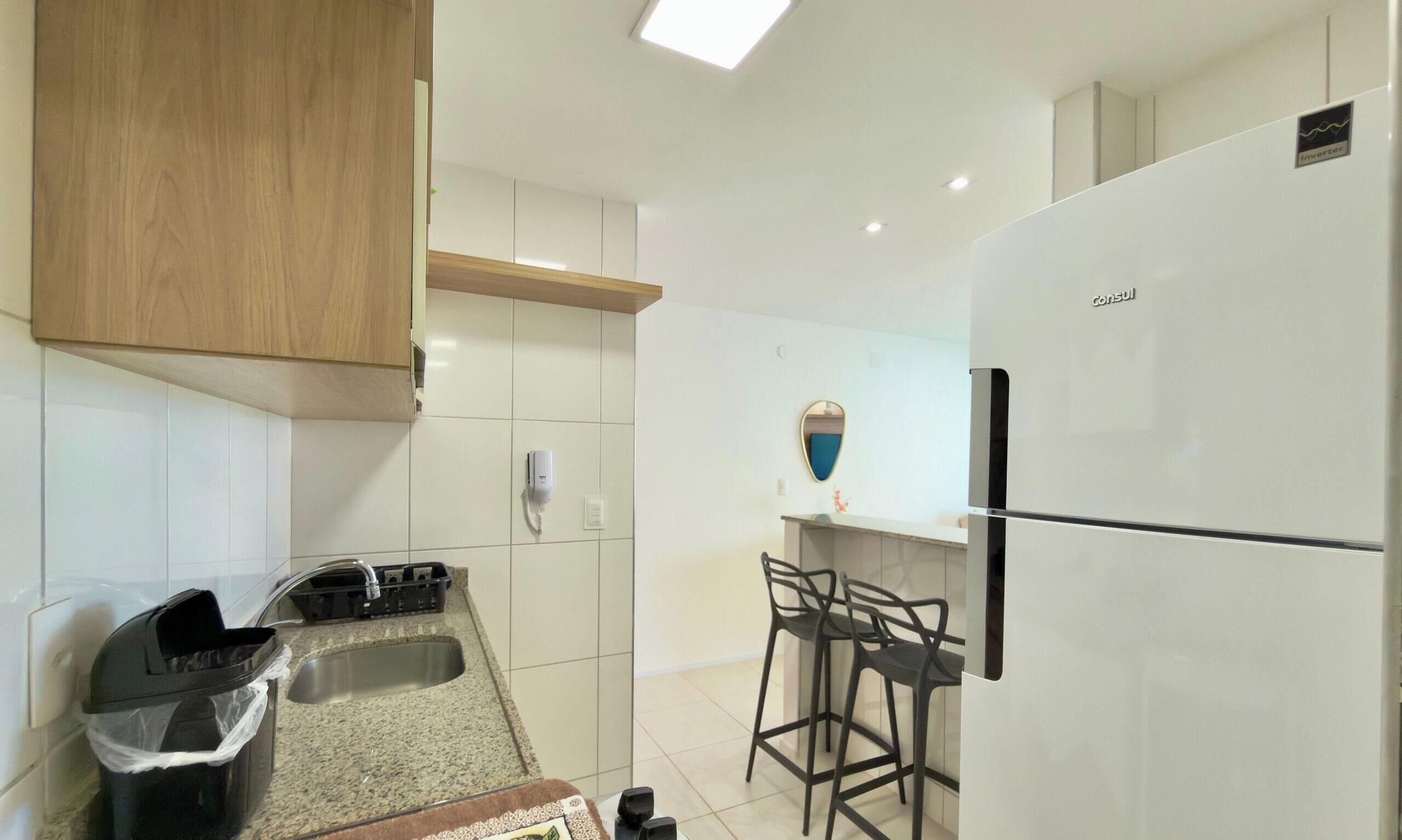 A modern kitchen with a refrigerator, a sink, and a dining area with chairs.