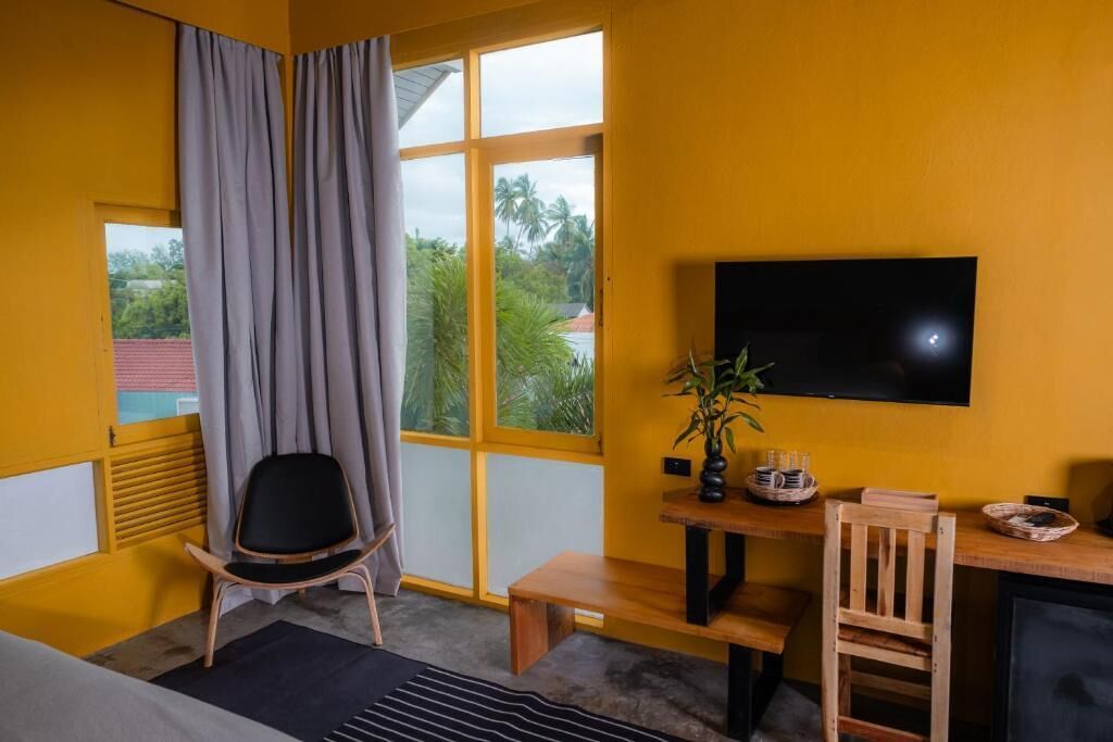 Una habitación con una cama, un escritorio con silla, un televisor y una ventana con cortinas.