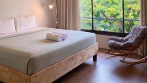 A bedroom with a large bed, a rocking chair, a window with a view of greenery, and a ceiling light. - Centerpoint Koh Phangan (Ko Pha-ngan)