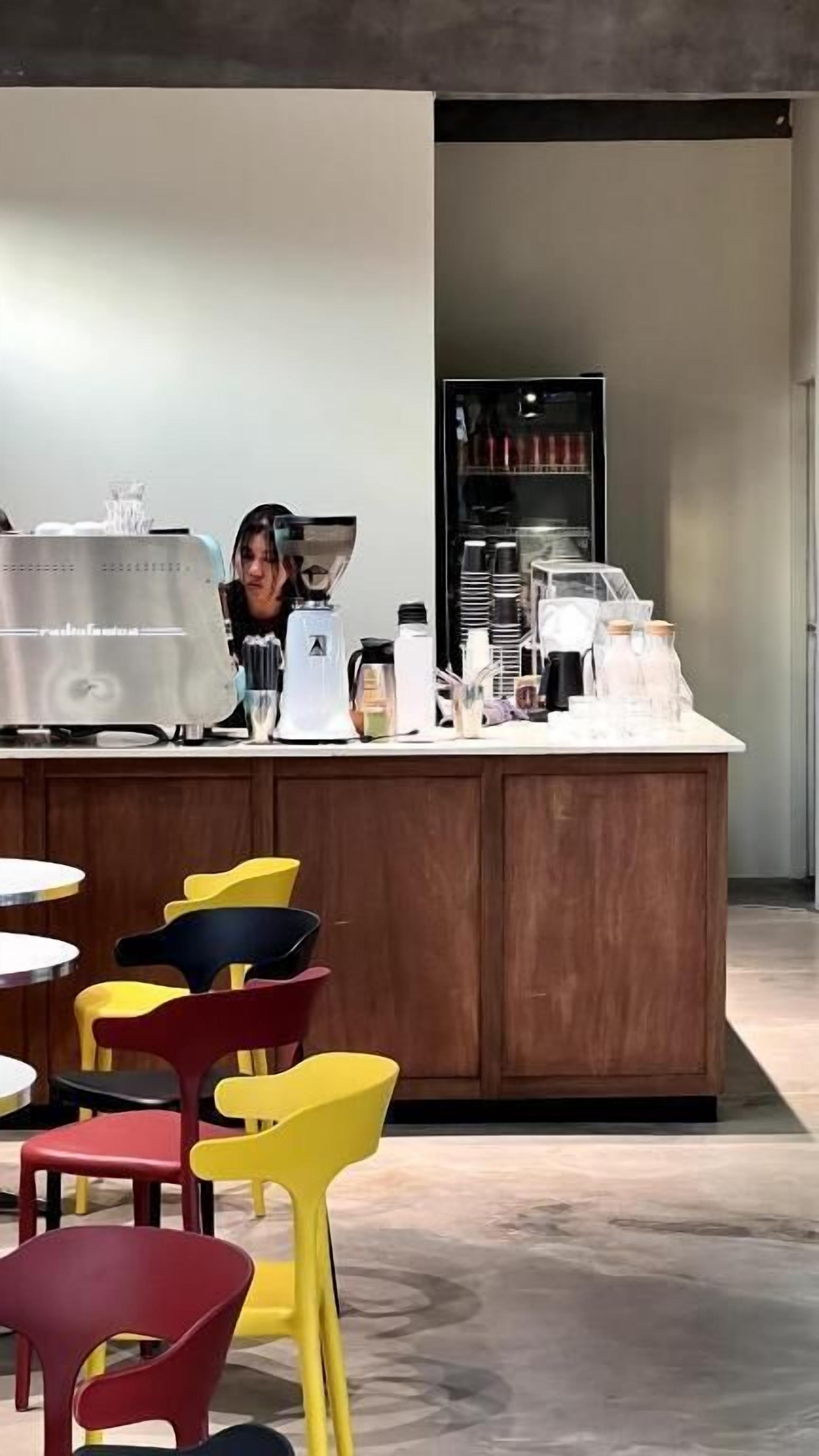 A modern cafe with a wooden counter, a coffee machine, and colorful chairs.