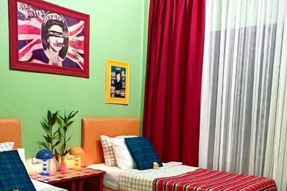 Une chambre avec deux lits, un mur vert, un rideau rouge et un drapeau Union Jack.