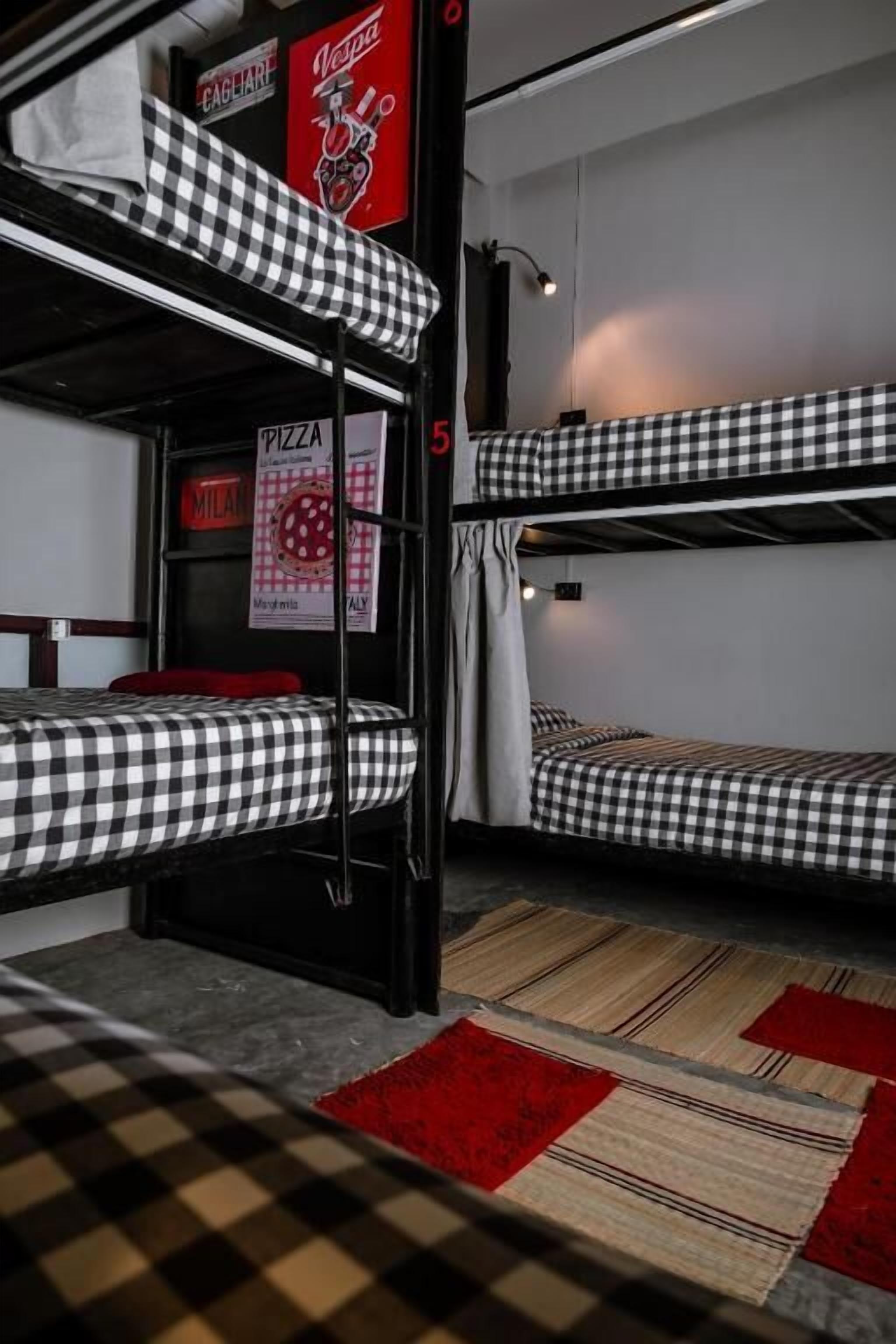 Ein Mehrbettzimmer mit karierten Laken, einer Pizzerias Speisekarte und einem rot-beigen Teppich.