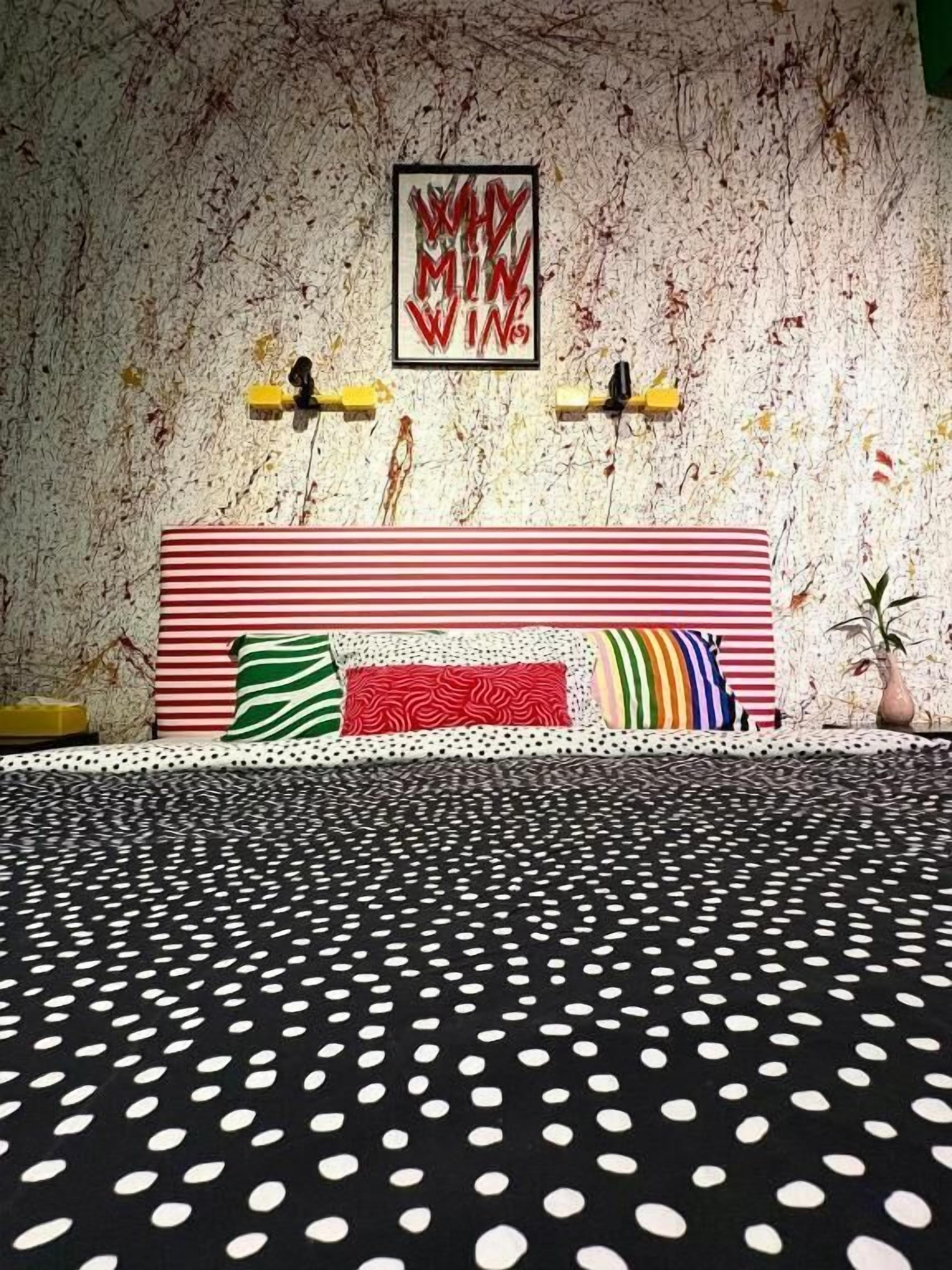 A room with a polka dot bedspread, a striped headboard, and a wall with a framed artwork.