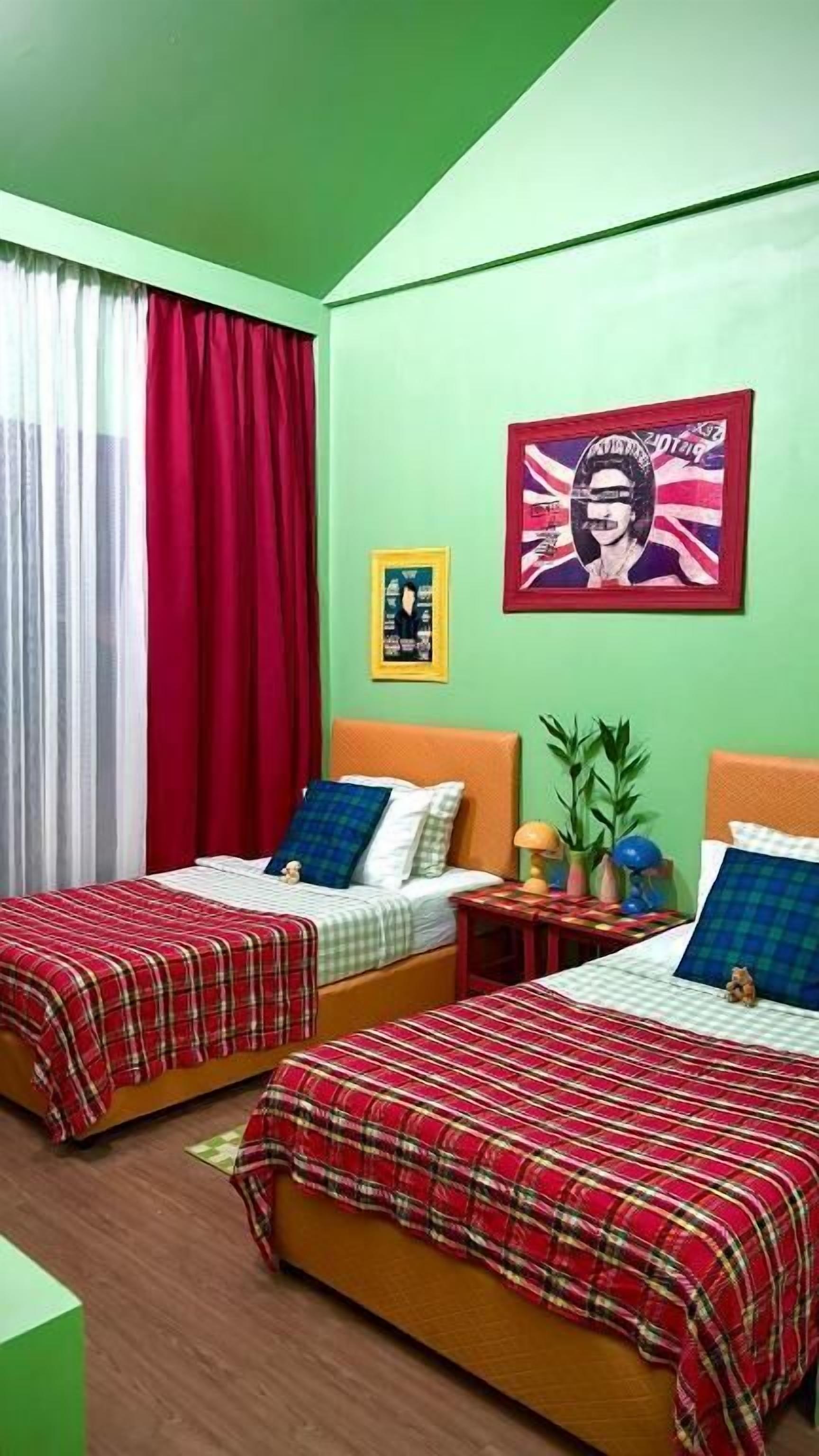 A room with two beds, a red curtain, a framed picture, and a small table with a plant.