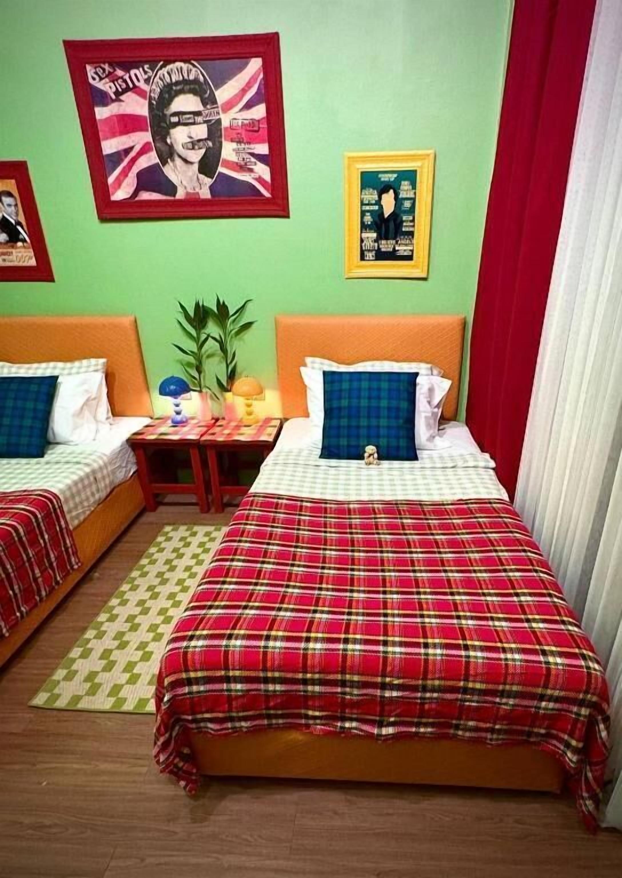 Una habitación con dos camas, una mesita de noche, una lámpara y un cartel en la pared.