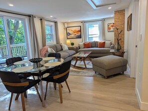 Ein modernes Wohnzimmer mit Sofa, Hocker, Esstisch, Stühlen und Kunstwerken.