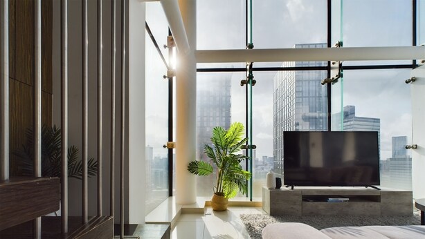 A modern bedroom with a large window, a flat-screen TV, and a potted plant. - Skyline 3BR Duplex | Pool, Gym & Parking (Manchester)