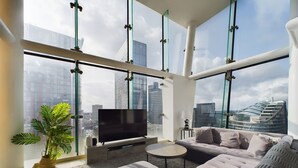 A modern living room with a large flat-screen TV, a sofa, a coffee table, and a potted plant. - Skyline 3BR Duplex | Pool, Gym & Parking (Manchester)