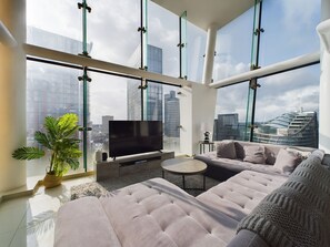 Ein modernes Wohnzimmer mit einem großen Flachbildfernseher, einer Couch, einem Couchtisch und einer Zimmerpflanze.