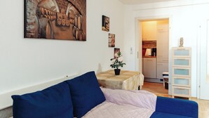A living room with a sofa, a table with a potted plant, and a kitchen in the background. - Lilians cozy apartment JAKO 3a (Graz)