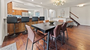 A modern kitchen with wooden cabinets, a dining area with a black table and brown chairs, and a staircase leading to another level.