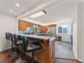 A modern kitchen with wooden cabinets, a stainless steel refrigerator, and a bar area with stools.