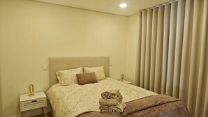 A bedroom with a bed, bedside tables, a nightstand, a rug, and a window with blinds. - 2 bedroom apartment 1 minute walk from Cortegaça beach - Refugio do Surf Cortegaça (Cortegaça)