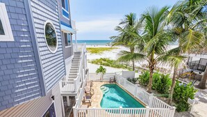 Ein Pool mit Blick auf den Strand, eine Treppe, die zum Pool führt, und ein weißer Zaun, der das Gebiet umgibt.
