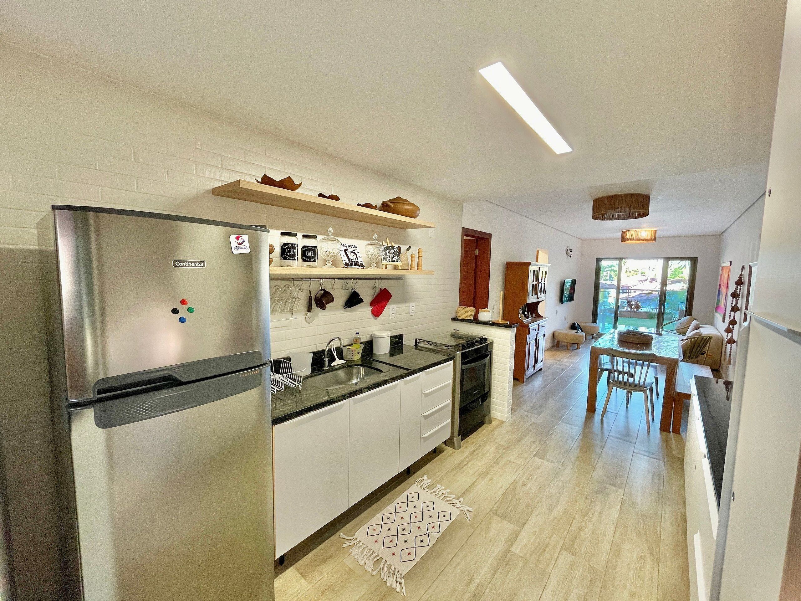 A modern kitchen with a refrigerator, stove, and white cabinets. There is a dining area with a table and chairs.