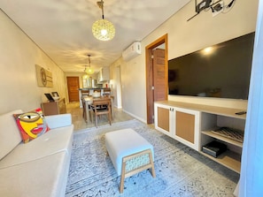 Ein kompakter Wohnbereich mit Sofa, Hocker, Esstisch, Stühlen, Fernseher und einer Küchenzeile.