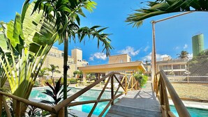 Une terrasse en bois qui mène à une piscine, avec vue sur un immeuble et des palmiers.