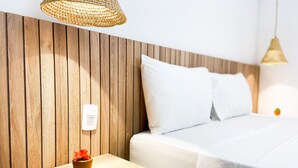 Une chambre d’hôtel avec une tête de lit en bois, une table de chevet ornée d’un vase de fleurs, un lit avec une literie blanche et un luminaire suspendu.