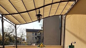 Un portico coperto con un tavolo apparecchiato per quattro persone, un'ampia urna decorativa e sullo sfondo edifici.