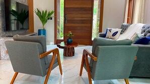 Ein Wohnzimmer mit grauem Sofa, zwei Sesseln, einem Holztisch, einem Fernseher und einer großen Holztür.