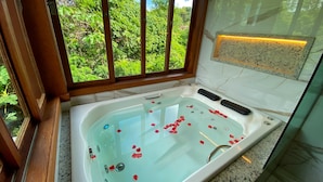 Ein Badezimmer mit einer Badewanne, einem Fenster mit Blick auf Grünflächen und einer Marmorwand.