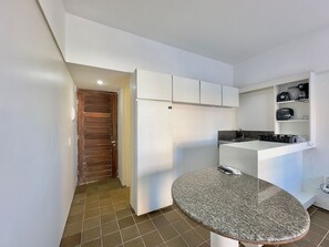 A kitchen with white cabinets, a granite countertop, and a wooden door. - Flats Tabajara Residence (Fortaleza)