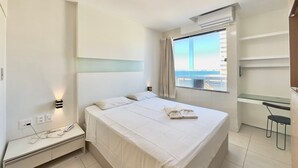 Habitación de hotel con cama, mesita de noche, lámpara, ventana con cortinas y escritorio con silla.