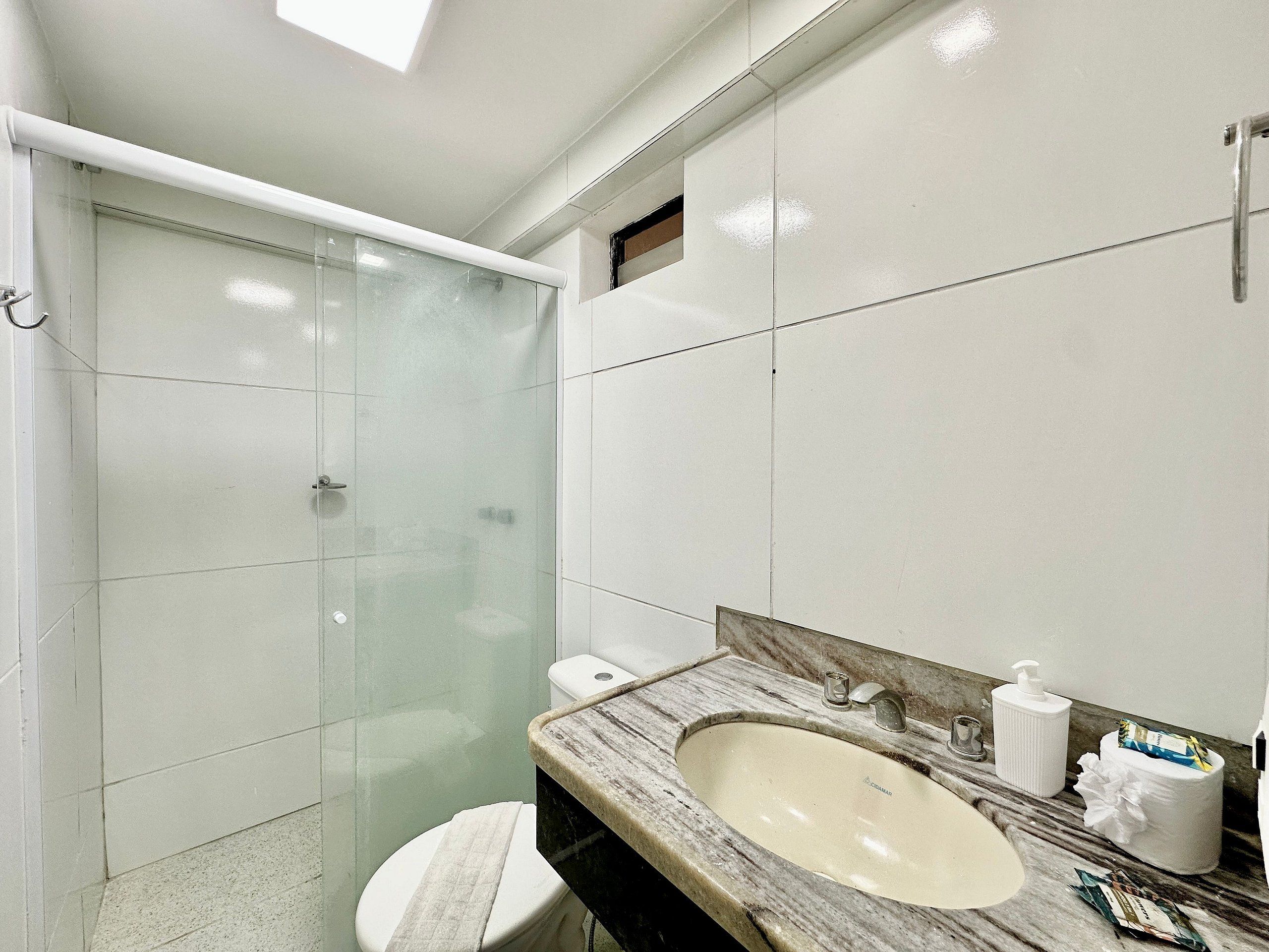 Ein Badezimmer mit Glasdusche, Toilette, Waschbecken mit Marmorplatte und Spiegel.