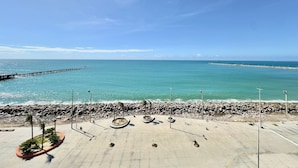 Un paseo marítimo con un muelle que se adentra en el mar, una costa rocosa y un cielo despejado.