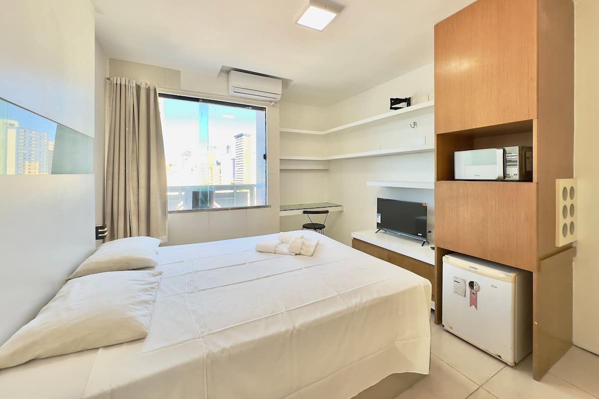A hotel room with a bed, a desk with a computer, a television, and a minibar.