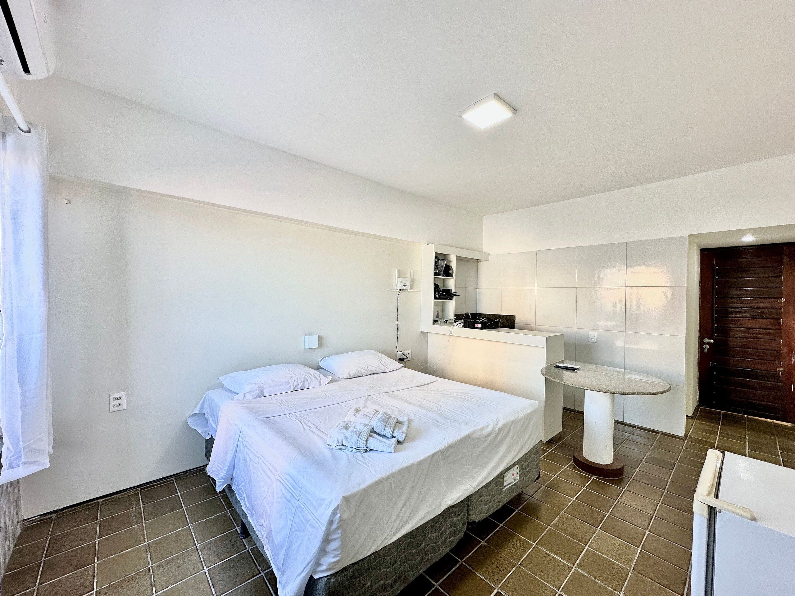Une chambre d’hôtel avec un lit, une petite table, un miroir et une porte.