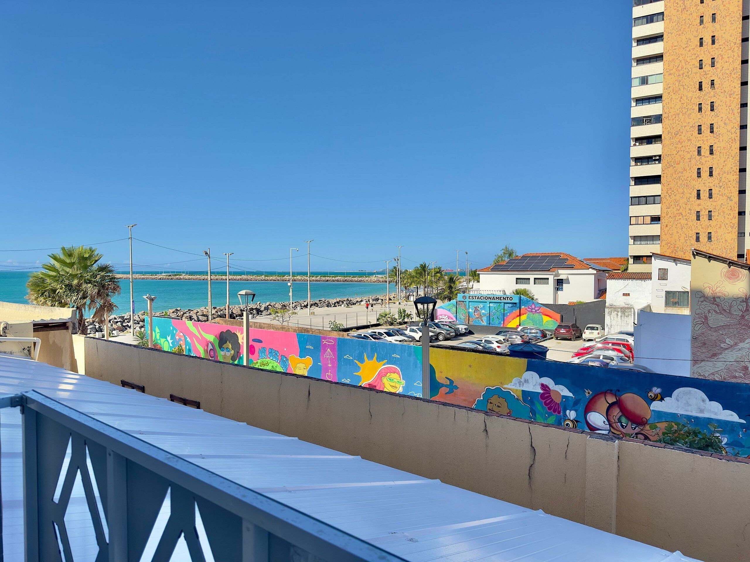 A coastal view with a colorful mural, a parking area, and a building labeled 'ESTACIONAMENTO.'