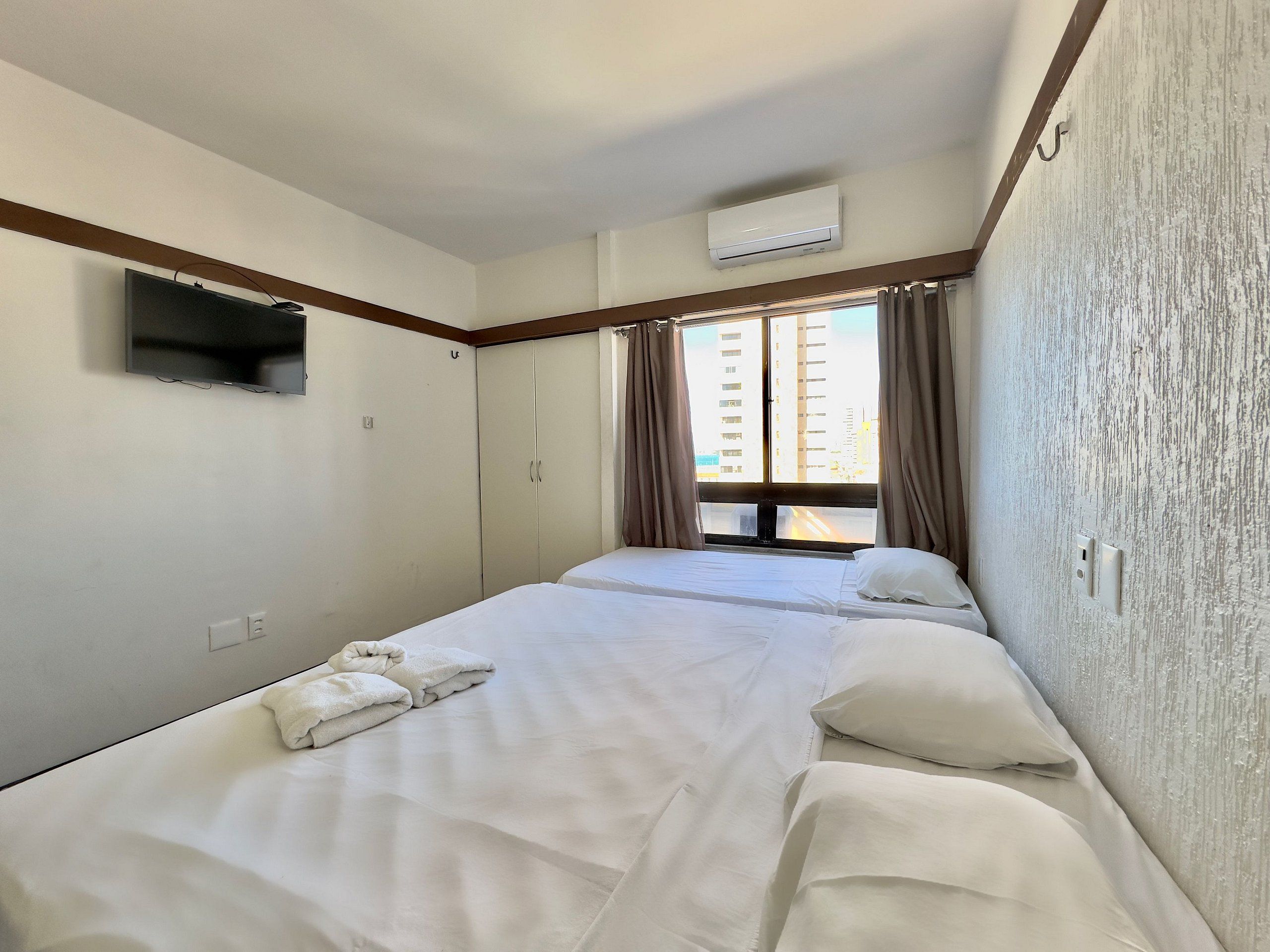 Una habitación de hotel con dos camas, televisión, aire acondicionado y una ventana con cortinas.