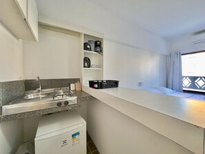 A kitchenette with a gas stove, sink, and a small refrigerator. There are shelves above the counter holding various items. - Flats Tabajara Residence (Fortaleza)