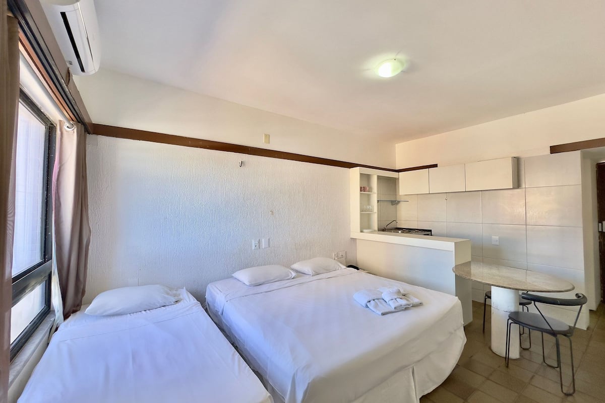 A hotel room with two beds, a kitchenette, a small table, and a window.