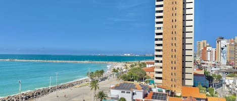 A high-rise building with a parking lot, a beach, and a clear blue sky.