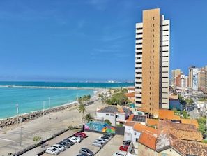 A high-rise building with a parking lot, a beach, and a clear blue sky. - Flats Tabajara Residence (Fortaleza)